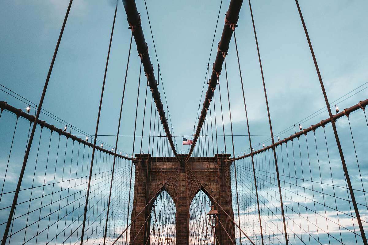 new york low angle photo of brown concrete suspension bridge under blue sky at daytime bridge